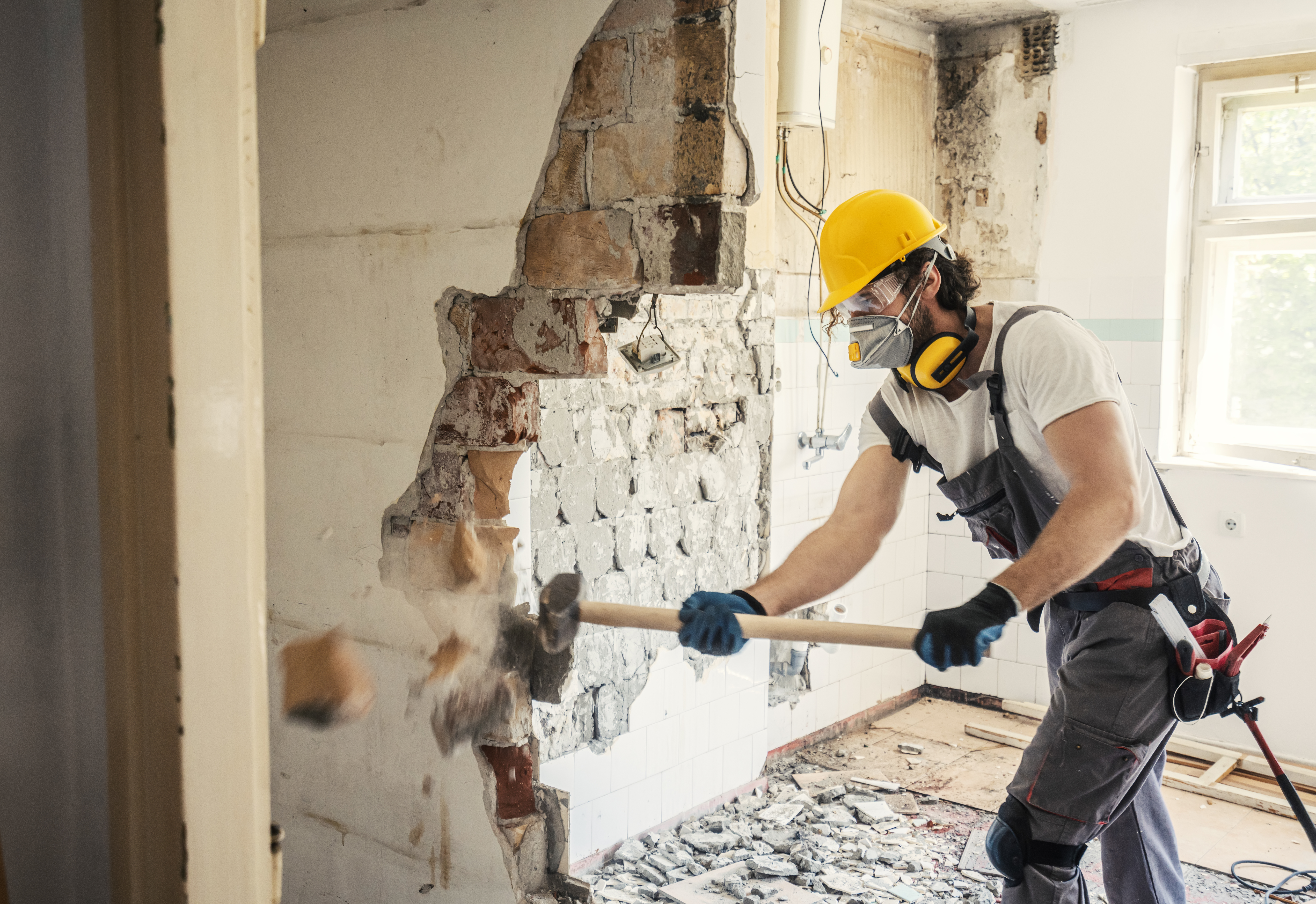 Contractor demolishing wall with sledgehammer
