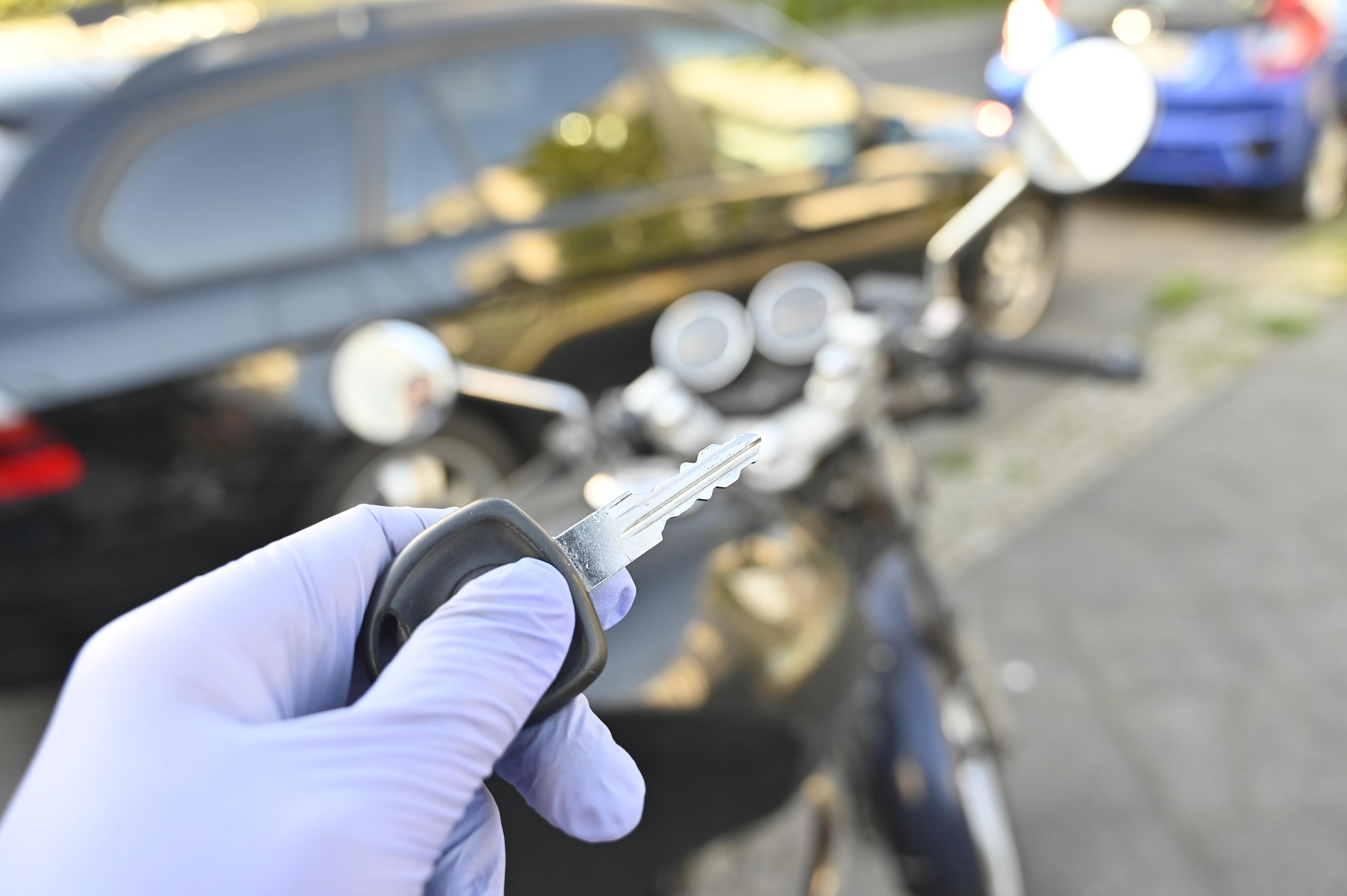 A glove-protected hand holds motorcycle key in front of motorcycle